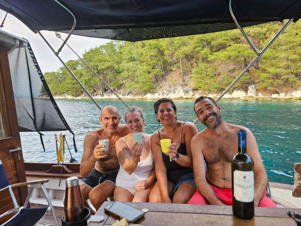 Friends laughing, fine wine, turquoise waters, lush pines meeting the sea in Vathi beach, Thassos with Odyssia Daily Cruise Tours